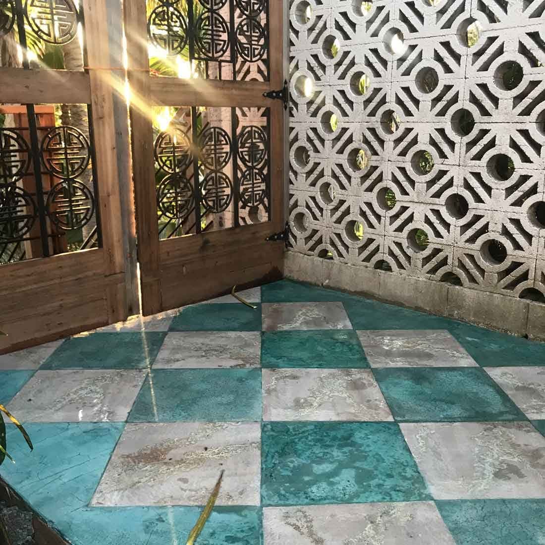 Turquoise and pale checkerboard stained patio beside a decorative block wall